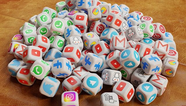 A pile of white dice, showcasing various social media and messaging app logos like Facebook, Instagram, and WhatsApp, symbolizes the complexity of managing social media budgets. They are scattered across a brown surface, reflecting the diverse platforms like YouTube, Twitter, and Reddit.