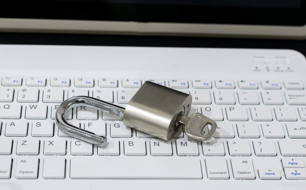 A padlock with a key inserted rests on a white computer keyboard, symbolizing the openness of website accessibility. The unlocked padlock stands in contrast to the tablet screen visible in the background, highlighting the importance of secure and inclusive digital environments.