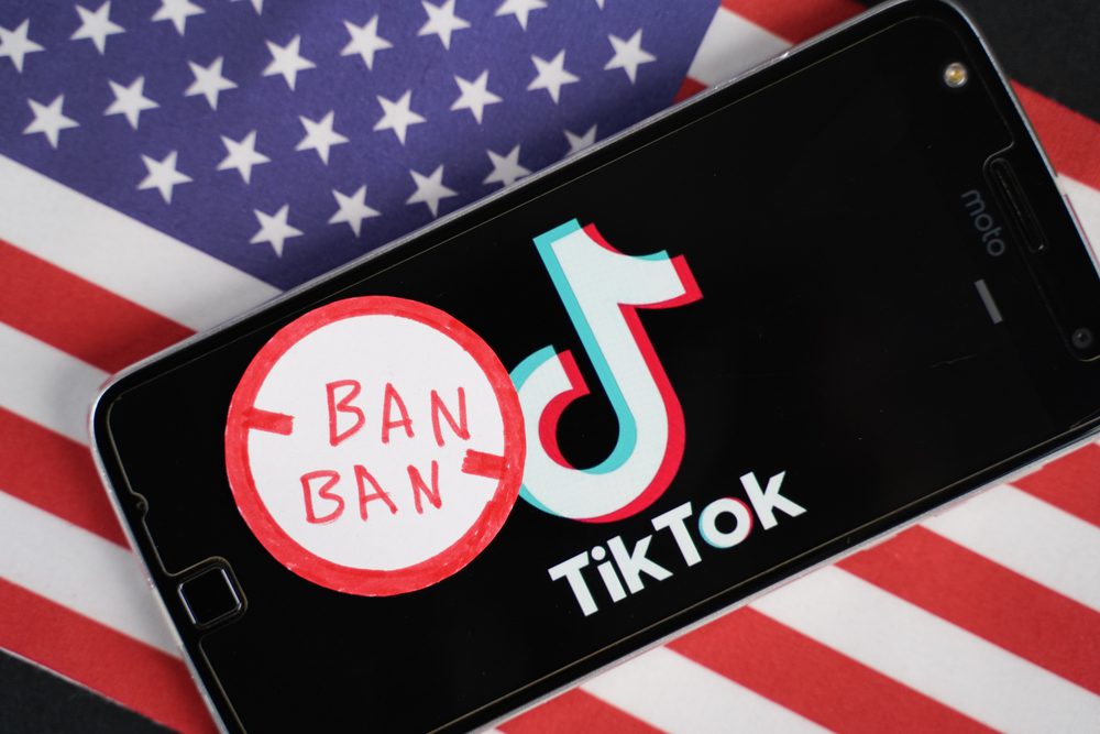 A smartphone displaying the TikTok logo rests on a U.S. flag. Nearby, a red circle with a line through it labeled BAN BAN symbolizes the idea of banning the app in the United States, highlighting the increasing interest in exploring alternatives to TikTok.