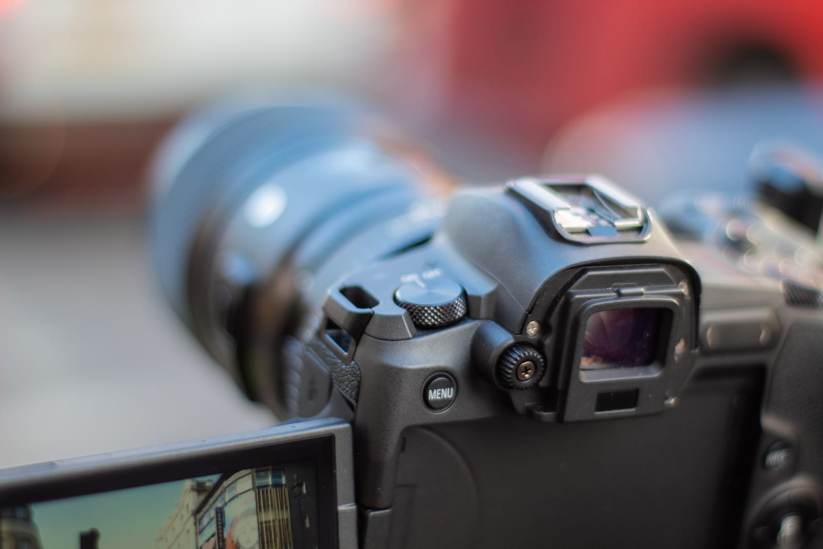 A close-up of a digital camera with a tilting LCD screen displaying a street scene; the camera’s buttons, viewfinder, and video controls are in focus, while the background is blurred.