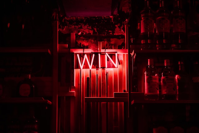 A neon sign reading WIN glows in red light, surrounded by shelves filled with bottles, creating a moody bar or nightclub atmosphere that seems to show promise for an unforgettable podcast.