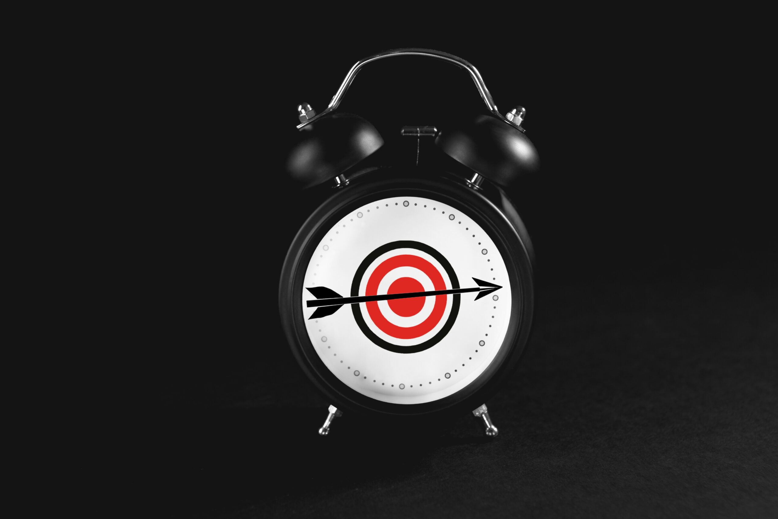 A black alarm clock with a target and an arrow hitting the bullseye on its face, reminiscent of a paused frame from a dramatic video, set against a dark background.